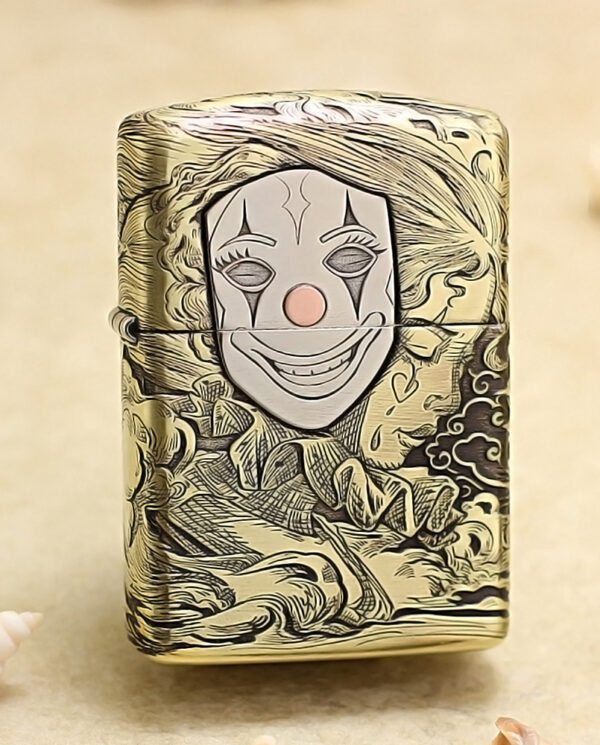 KZ154 Engraved metal lighter with a smiling clown face on the front and decorative swirling patterns in gold tones.