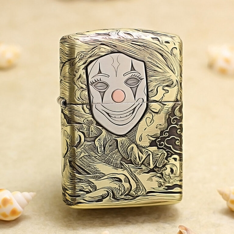 Engraved metal lighter with a smiling clown face on the front and decorative swirling patterns in gold tones.