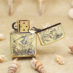 Gold engraved Zippo lighter with a mermaid sea motif, open lid, resting on sandy beach with seashells nearby.