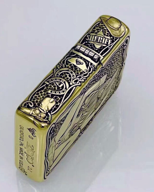 KZ157-03 Gold engraved Zippo-style lighter with ornate black patterns and a hinged top, photographed from a diagonal side angle.