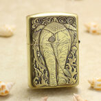 Decorative brass lighter with a raised elephant design, standing on sand with seashells nearby (beach motif).