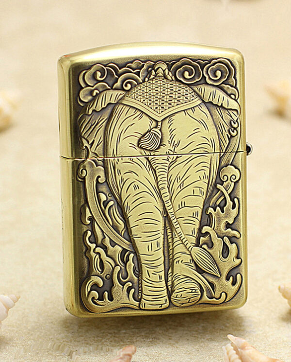 KZ158-01 Decorative brass lighter with a raised elephant design, standing on sand with seashells nearby (beach motif).