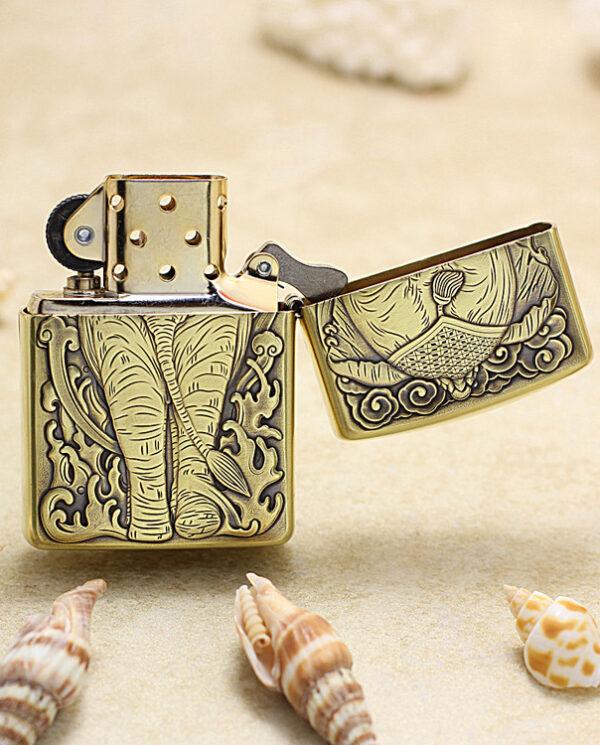 KZ158-03 Brass Zippo lighter with intricate elephant engraving, open lid, on a sandy beach among seashells.