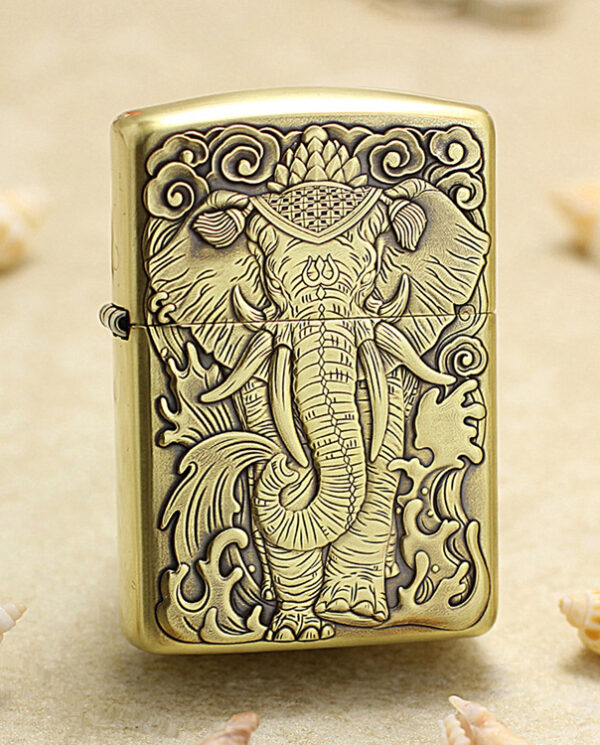 KZ158 Brass Zippo-style lighter with a detailed embossed elephant deity design, placed on a sandy surface with seashells nearby.