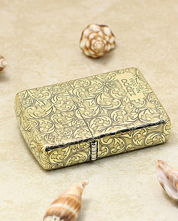 KZ159-04 Gold-toned lighter with intricate floral scrollwork on a sandy surface, surrounded by seashells.
