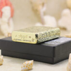Shiny Zippo lighter with an ornate swirling pattern resting on a black box.
