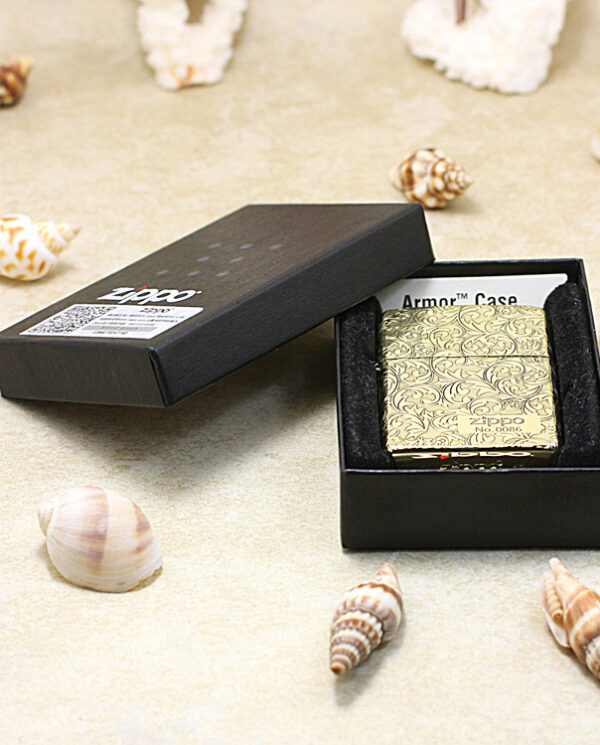 KZ159-06 Gold patterned Zippo lighter in a black gift box on a sandy surface with seashells scattered around.