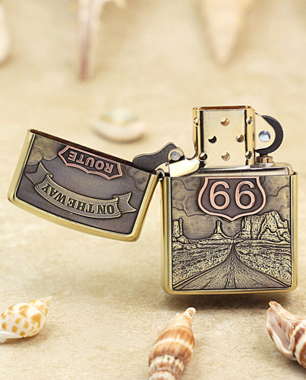 KZ160-02 Bronze Zippo lighter with Route 66 shield and desert road engraving, lid open, on a sandy surface with seashells nearby.