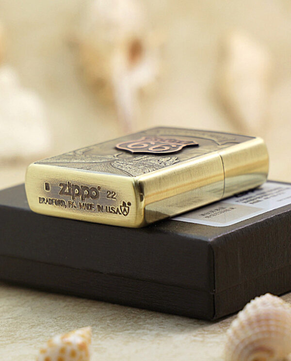 KZ160-05 Gold Zippo lighter resting on a black box, with seashells in the foreground