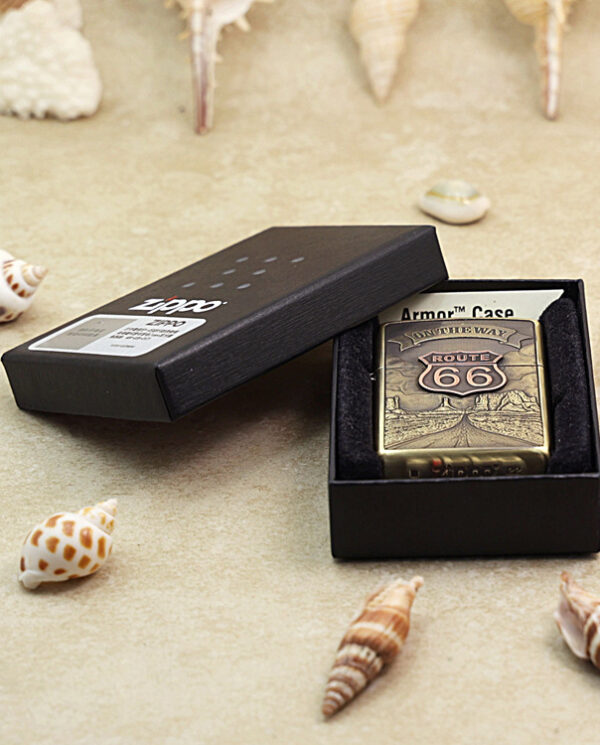 KZ160-06 Brass Zippo lighter with Route 66 design in an open black presentation box, surrounded by seashells.