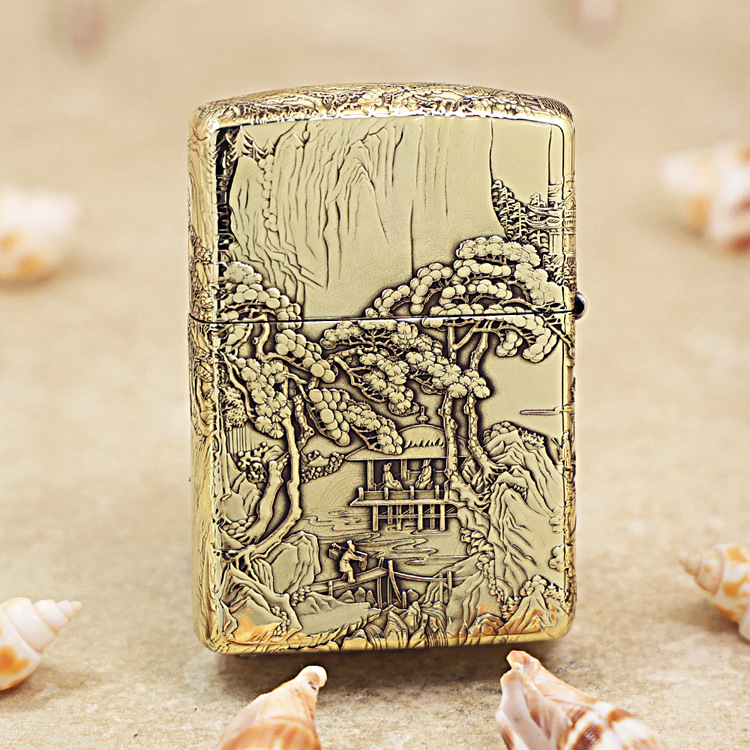 Gold engraved lighter with a detailed landscape scene of trees, a pavilion, and a boat on a river in relief artwork.
