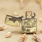 Gold engraved Zippo-style lighter open to reveal the wheel, resting on sand with seashells nearby.