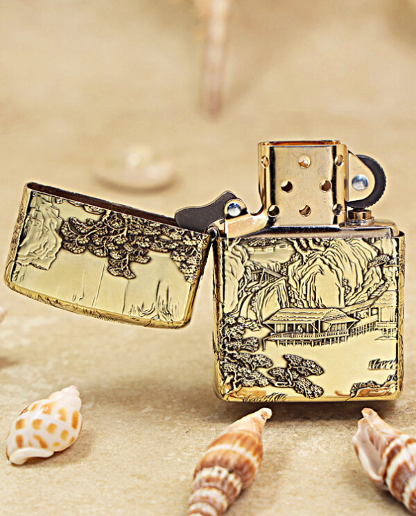 KZ162-02 Gold engraved Zippo-style lighter open to reveal the wheel, resting on sand with seashells nearby.