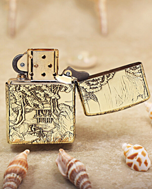 KZ162-03 Gold engraved Zippo lighter with open lid on sandy beach, surrounded by seashells.