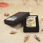 Black Zippo lighter in its open black box on a sandy beach with seashells nearby.