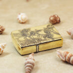 Gold engraved lighter with a rose motif rests on sandy beach among seashells.