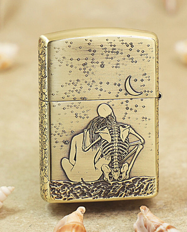 Gold lighter with a skeleton couple embracing on a sandy beach under a crescent moon.