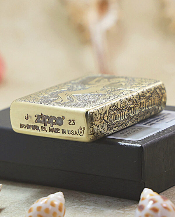 Gold Zippo lighter with floral etching resting on a black box, showing Zippo branding and 'Made in USA' text at the base.
