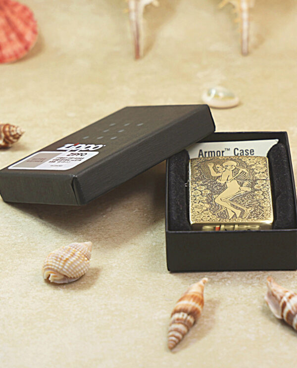 Gold-toned Zippo lighter with an engraved man running design in an open black box on a sandy beach with seashells nearby.