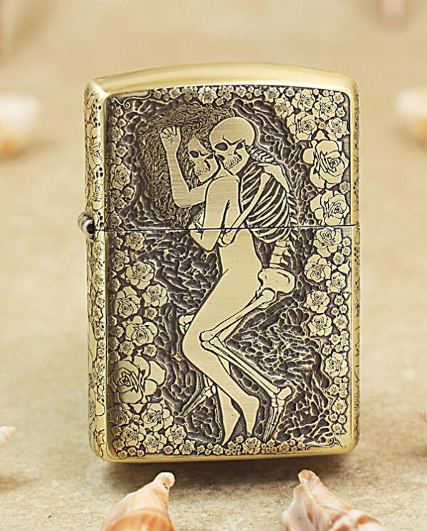 Gold Zippo lighter with an etched skeleton couple dancing among roses on a floral background, decorative and ornate.