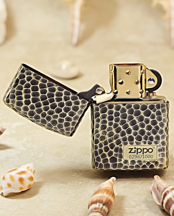 KZ175-02 Snakeskin-pattern Zippo lighter with open lid on a sandy beach, surrounded by seashells and shells.