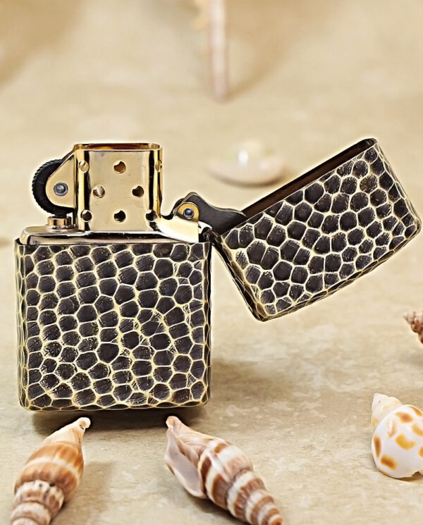 KZ175-03 Gold and black snakeskin-pattern lighter with open lid on a sandy surface, surrounded by seashells