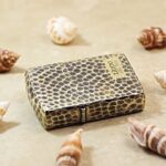 Snakeskin texture Zippo Armor lighter lying flat among seashells