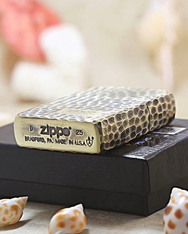 KZ175-05 Zippo lighter with a snakeskin pattern resting on a black box, with small seashells in the foreground, stamped 'Made in USA'.