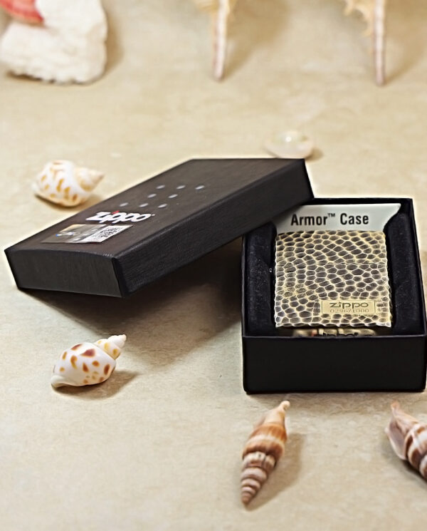 KZ175-06 Square, snake-skin textured Zippo Armor Case inside an open black presentation box on a beige surface with scattered seashells nearby.