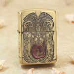 Biomechanical alien engraving with red-brown accent on brass Zippo Armor lighter, front view
