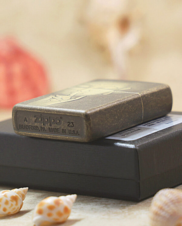 KZ179-05 Bronze Zippo lighter resting on a black box, with seashells and a soft beachy background.