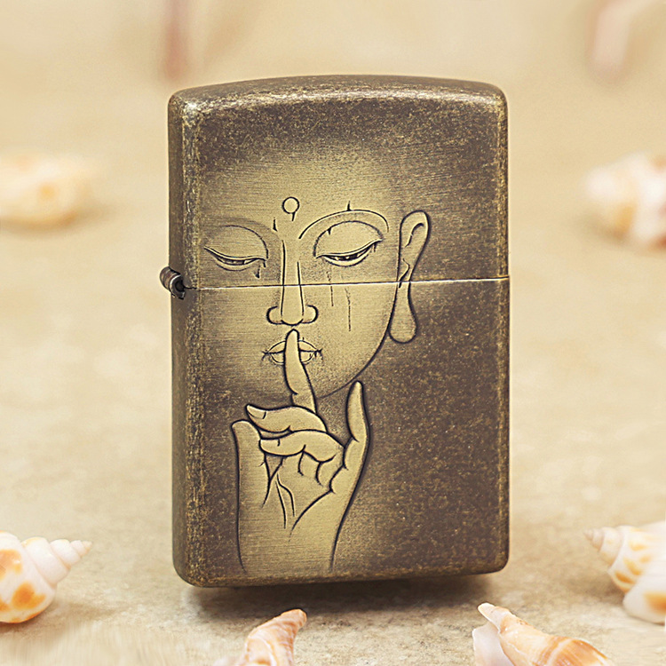 Bronze metal lighter with a line drawing of a person holding a finger to their lips, signaling 'shh', on a sandy surface with seashells nearby.