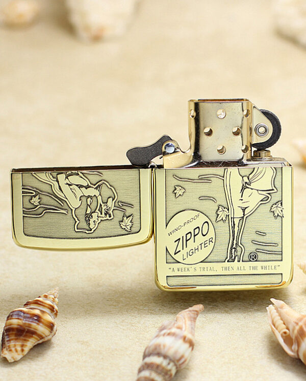 KZ183-02 Gold Zippo lighter open, engraved beach scene with seashells around it on sand. This lighter shows a wind-proof design and vintage artwork.