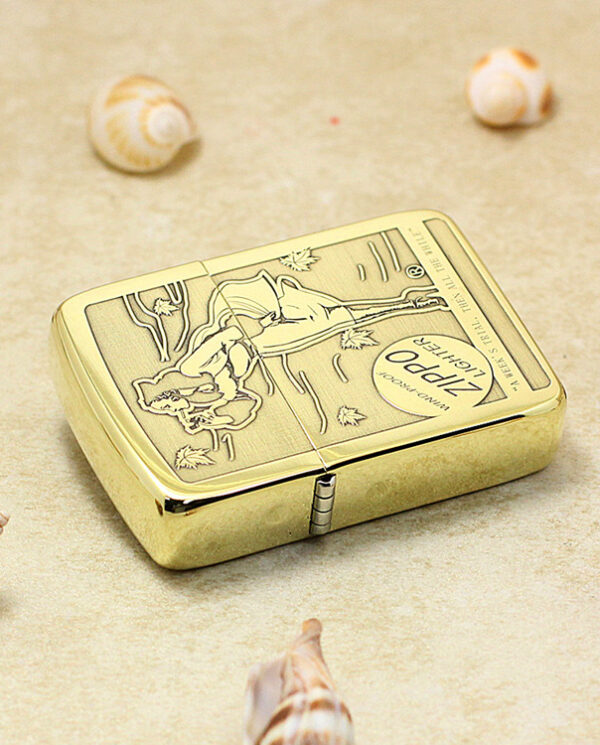 KZ183-04 Gold Zippo lighter with engraved design lying on a sandy surface, surrounded by seashells.