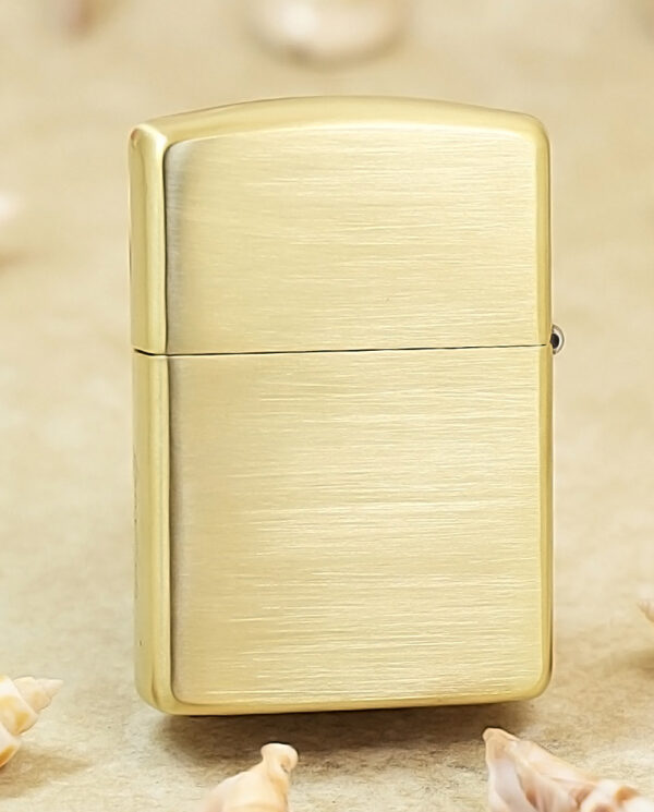 KZ184-01 Brushed gold Zippo-style lighter standing upright on a sandy surface with scattered seashells nearby