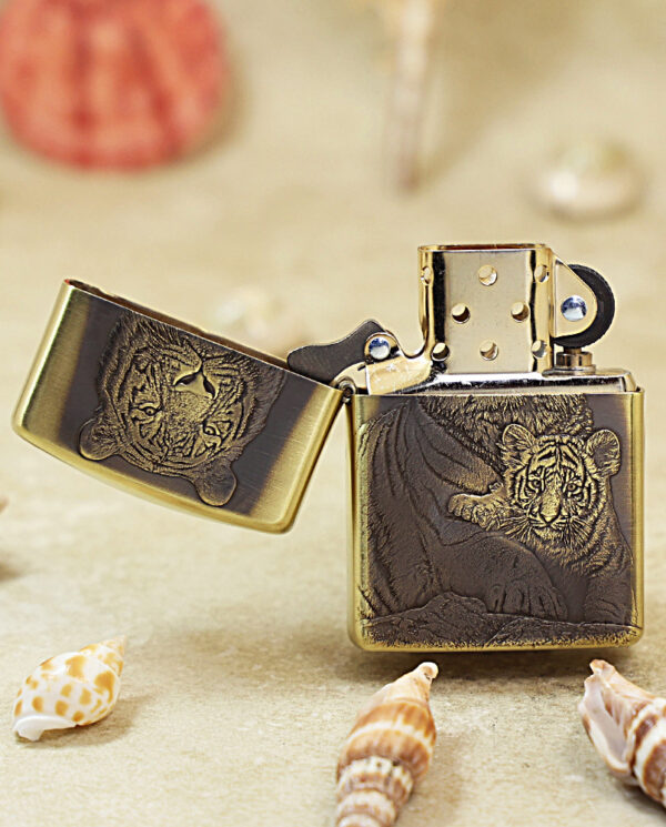 KZ184-02 Brass Zippo lighter with a carved tiger design, open on a sandy surface with seashells nearby.