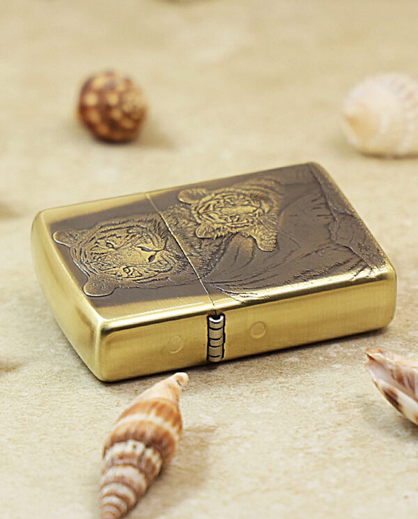 KZ184-04 Gold Zippo lighter with a tiger engraving on a sandy surface among seashells.