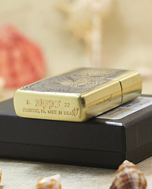 KZ184-05 Brass Zippo lighter with engraved pattern on a black box, beach scene with seashells in the foreground.