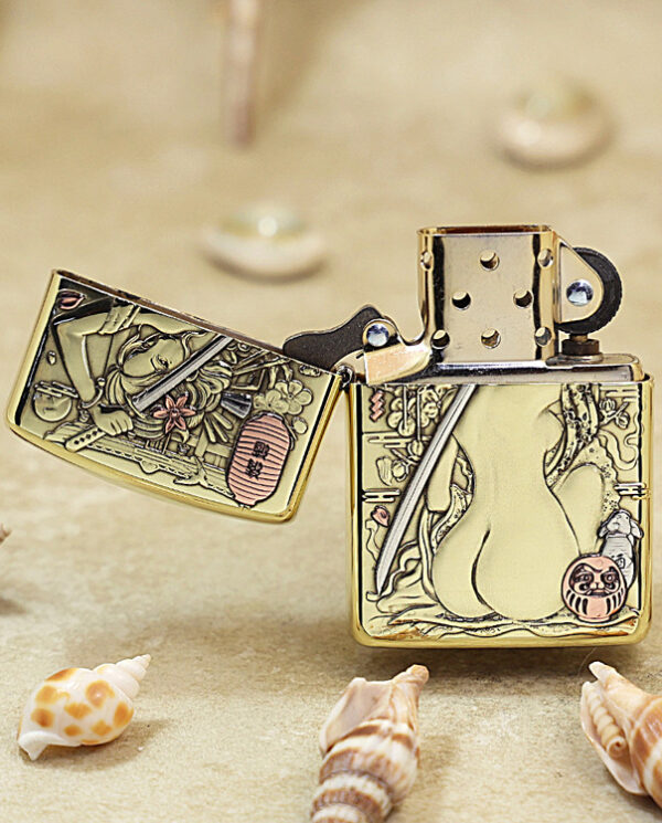 KZ189-02 Gold-tone Zippo lighter with intricate Asian-inspired engravings, lid open, resting on sand among seashells.