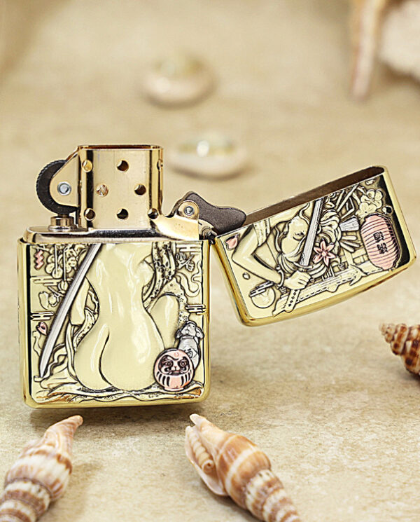 KZ189-03 Gold Zippo lighter with intricate Asian-inspired engravings, open to show the lid and flint wheel, surrounded by seashells on a sandy surface.