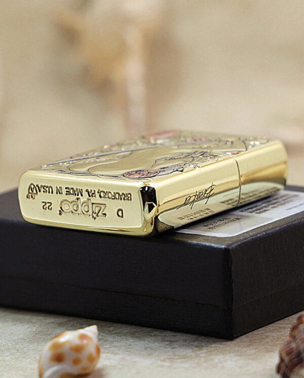 KZ189-05 Gold Zippo lighter resting on a black box with seashells nearby, close-up product shot.