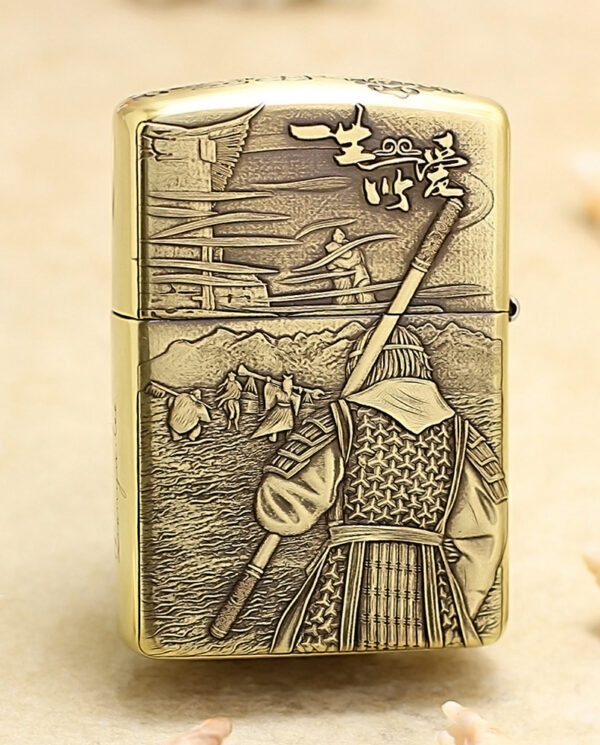 KZ190-01 Gold Zippo-style lighter with a backward-facing samurai in armor, holding a spear, set against a mountainous village scene in relief on the surface.