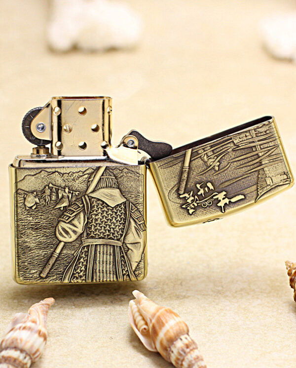 KZ190-03 Brass Zippo lighter with samurai engraving on sand, lid open showing flint wheel and interior detail.