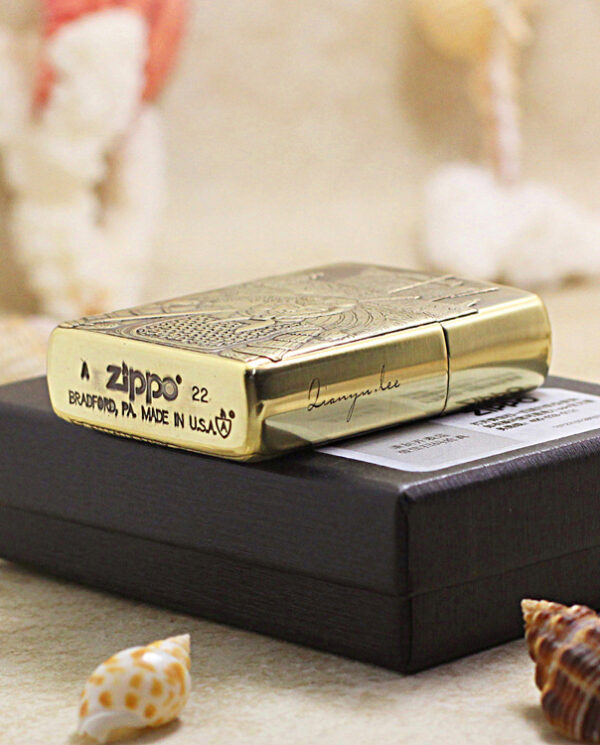 KZ190-05 Gold Zippo lighter with engraved pattern resting on a black box, shell decor around it.