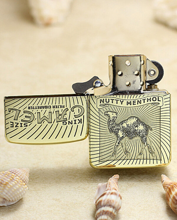 Gold-tone Zippo lighter with camel engraving and 'Nutty Menthol' banner, open on a sandy beach with seashells.