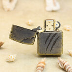 Vintage brass lighter with a dark cracked leather cover and open lid on sandy beach with seashells nearby.