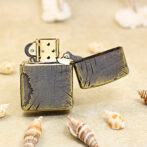 Bronze vintage lighter with an open lid on a sandy beach, surrounded by seashells.