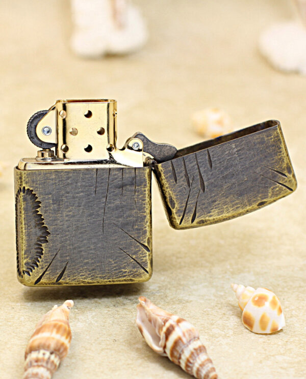 Bronze vintage lighter with an open lid on a sandy beach, surrounded by seashells.