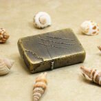 Bronze vintage lighter on sand among seashells, with three scratch marks on its lid.