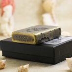 Brass Zippo lighter resting on a black box with seashells in the foreground, close-up shot of the lighter's worn surface.